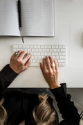 Person typing on a white keyboard with a notebook open on a desk